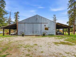 This property features a large, rustic metal barn with expansive covered parking areas on either side, perfect for storing vehicles or equipment.