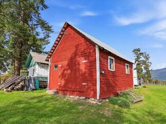 This charming red barn, set against a backdrop of lush green grass and a clear blue sky, offers a rustic aesthetic perfect for any rural property.