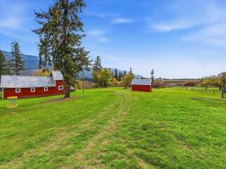Discover this picturesque rural property featuring two charming red barns set against a backdrop of rolling hills and mature trees.