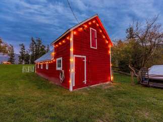 Experience rustic charm with this vibrant red barn, beautifully illuminated by festive string lights.
