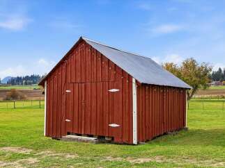 Discover this charming red barn, a quintessential piece of rural architecture, set against a backdrop of rolling hills and a clear blue sky.