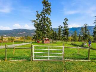 Experience rural living at its finest with this picturesque property, featuring a charming red barn and a smaller red shed nestled amongst mature trees.