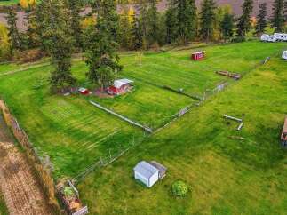 Discover this charming rural property featuring multiple red outbuildings, including a main barn with an overhang, and a smaller red shed.