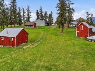 Discover this charming rural property featuring multiple red barns with silver roofs, set against a backdrop of lush green fields and mature trees.