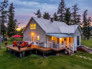 Experience the charm of this picturesque home, featuring a spacious wooden deck perfect for outdoor entertaining, complete with comfortable seating and a vibrant red umbrella.
