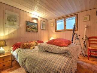 Cozy wooden paneled bedroom featuring a comfortable bed with plaid bedding and plush toys.