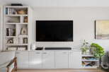 This modern living room features a sleek, wall-mounted television above a minimalist white media console, offering ample storage with its handleless cabinets.