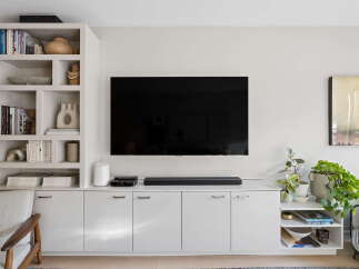 This modern living room features a sleek, wall-mounted television above a minimalist white media console, offering ample storage with its handleless cabinets.