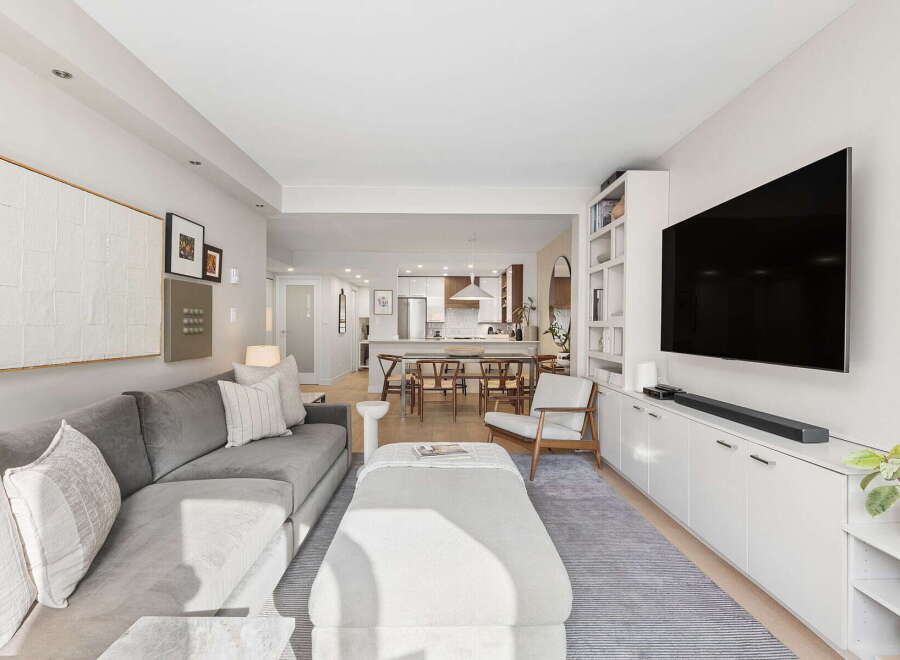 This open-concept living and dining area features a spacious sectional sofa, a large ottoman, and a wall-mounted TV above a sleek white media console.