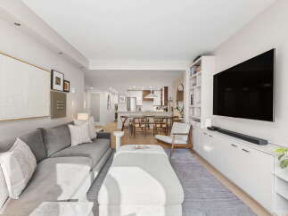 This open-concept living and dining area features a spacious sectional sofa, a large ottoman, and a wall-mounted TV above a sleek white media console.
