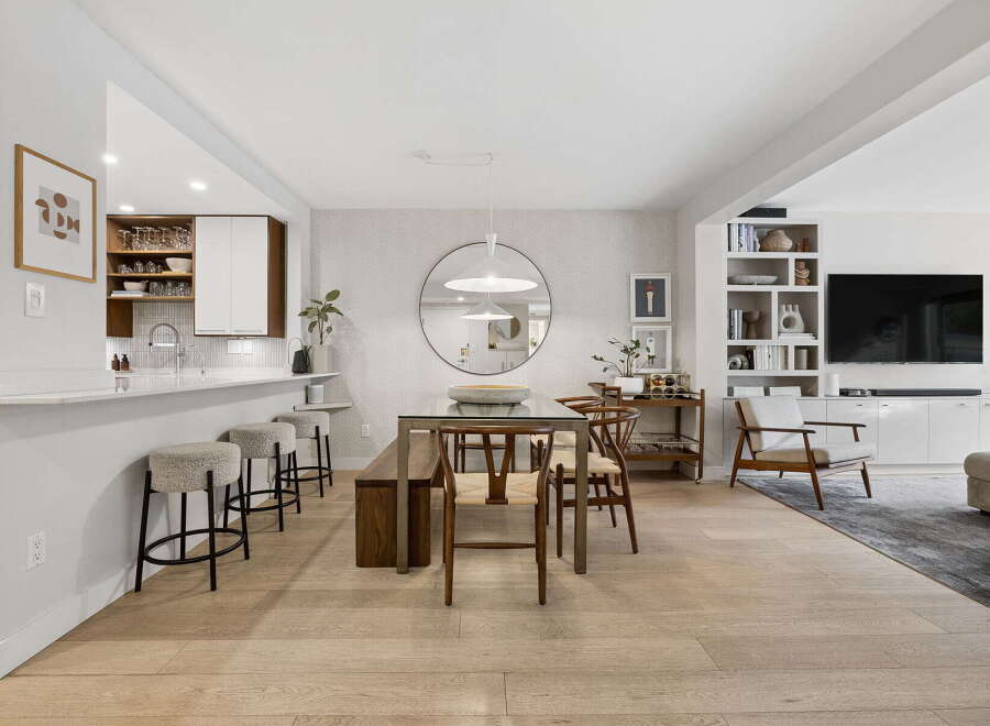This open-concept living space features a modern kitchen with a breakfast bar, a stylish dining area with a glass-top table and wooden chairs, and a cozy living room with a built-in entertainment center.