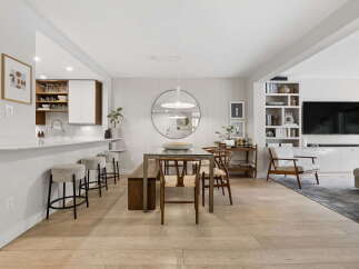 This open-concept living space features a modern kitchen with a breakfast bar, a stylish dining area with a glass-top table and wooden chairs, and a cozy living room with a built-in entertainment center.