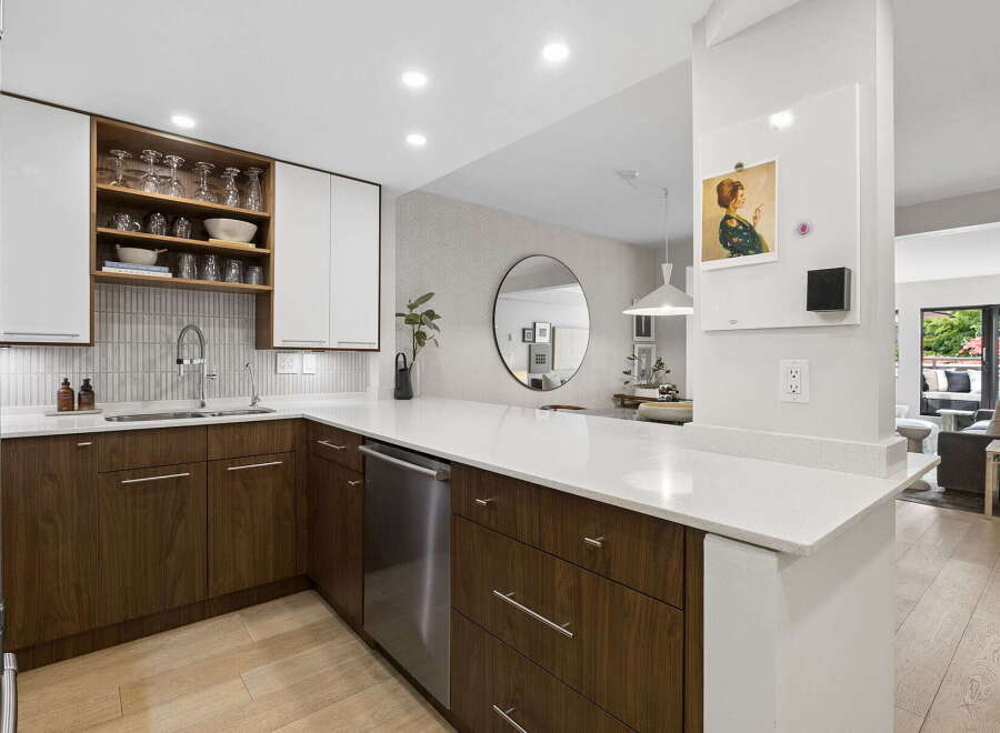 This modern kitchen boasts sleek white upper cabinets and rich walnut lower cabinets, complemented by a sparkling quartz countertop.