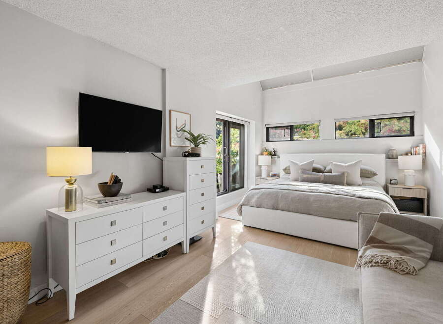 This modern bedroom features a king-size bed with a white upholstered headboard, complemented by a plush grey duvet and an array of decorative pillows.