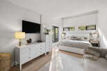 This modern bedroom features a king-size bed with a white upholstered headboard, complemented by a plush grey duvet and an array of decorative pillows.