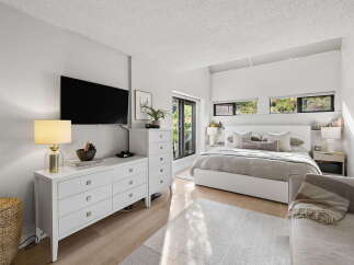 This modern bedroom features a king-size bed with a white upholstered headboard, complemented by a plush grey duvet and an array of decorative pillows.