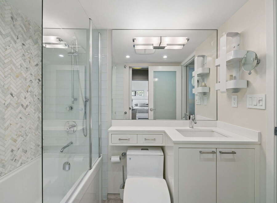 This modern bathroom features a sleek white vanity with ample storage, a clean white toilet, and a bathtub with a glass enclosure.