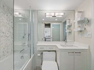 This modern bathroom features a sleek white vanity with ample storage, a clean white toilet, and a bathtub with a glass enclosure.