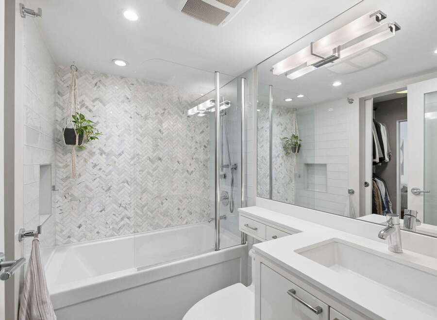This modern bathroom features a sleek white bathtub with a herringbone tile accent wall and a glass shower enclosure.