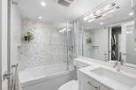 This modern bathroom features a sleek white bathtub with a herringbone tile accent wall and a glass shower enclosure.