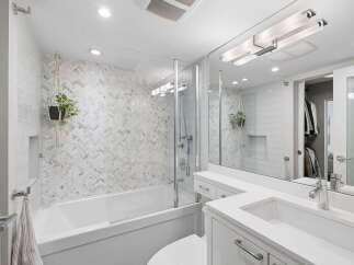 This modern bathroom features a sleek white bathtub with a herringbone tile accent wall and a glass shower enclosure.