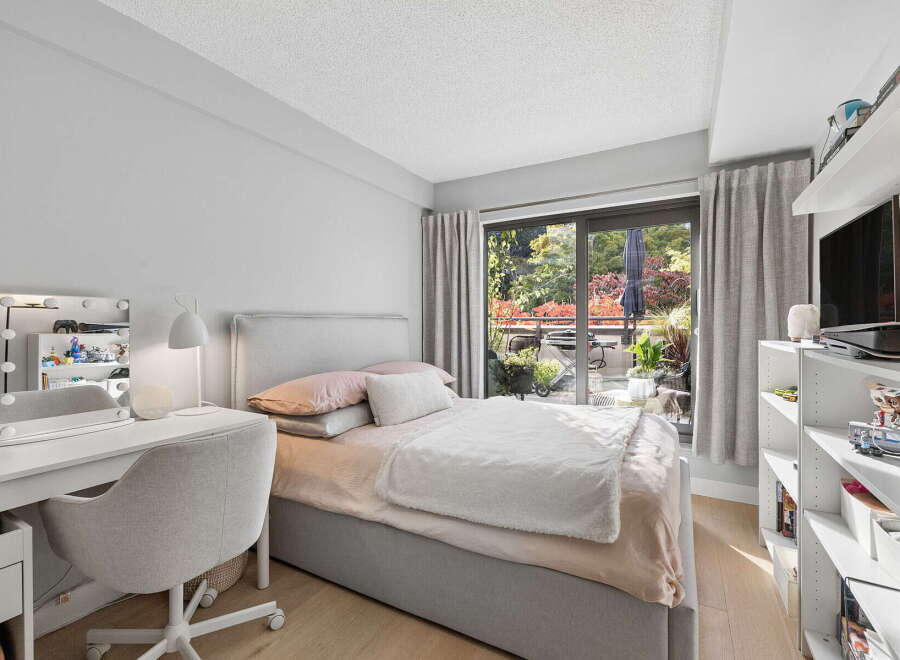 This cozy bedroom features a comfortable bed with plush bedding, a stylish vanity with a lighted mirror, and a functional desk area.