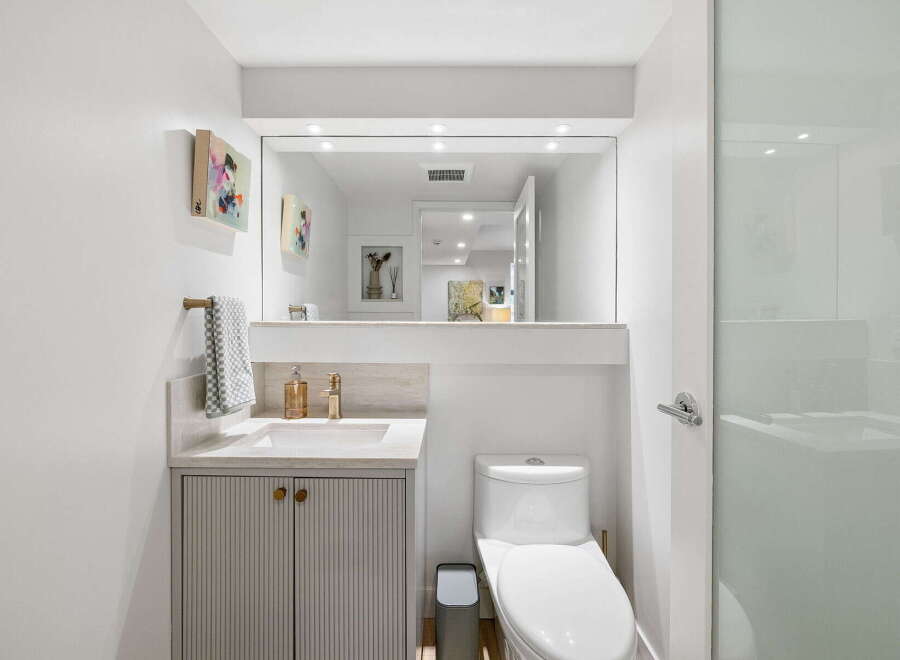 This modern bathroom features a sleek vanity with fluted cabinetry and gold hardware, complemented by a marble countertop and a brass faucet.