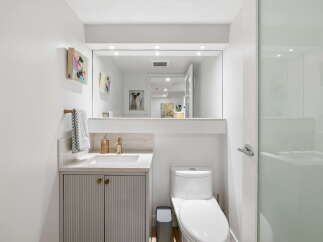 This modern bathroom features a sleek vanity with fluted cabinetry and gold hardware, complemented by a marble countertop and a brass faucet.