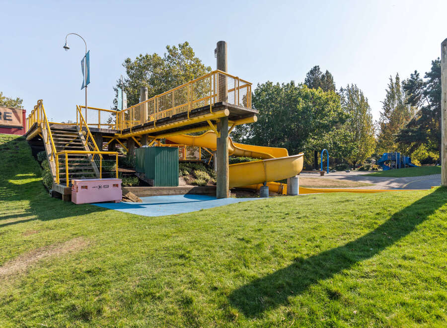 Discover this vibrant playground featuring a bright yellow slide and an elevated wooden walkway with safety railings.