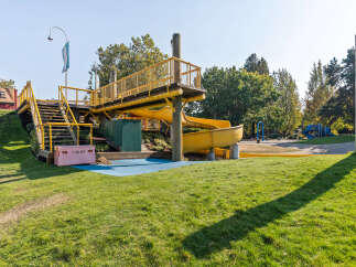 Discover this vibrant playground featuring a bright yellow slide and an elevated wooden walkway with safety railings.