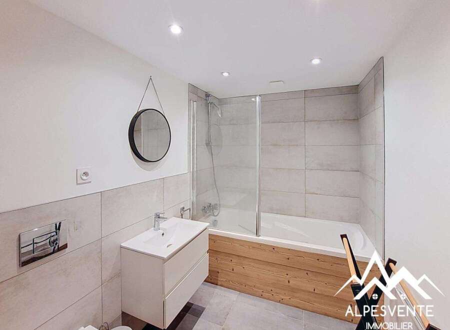This modern bathroom features a sleek white vanity with a vessel sink, complemented by a round black-framed mirror and a wall-mounted faucet.