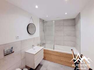 This modern bathroom features a sleek white vanity with a vessel sink, complemented by a round black-framed mirror and a wall-mounted faucet.