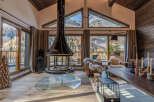 Experience the ultimate mountain retreat in this stunning living room, featuring a dramatic suspended fireplace and panoramic windows that showcase breathtaking autumnal forest and snow-capped peaks.