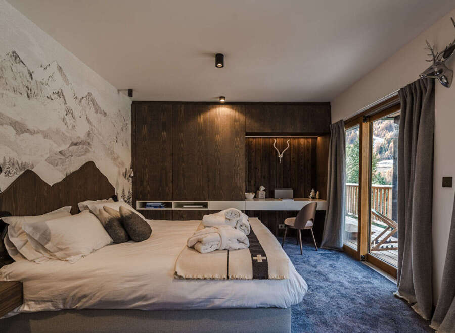 Experience alpine luxury in this beautifully appointed bedroom, featuring a striking mountain mural and rich wood paneling.