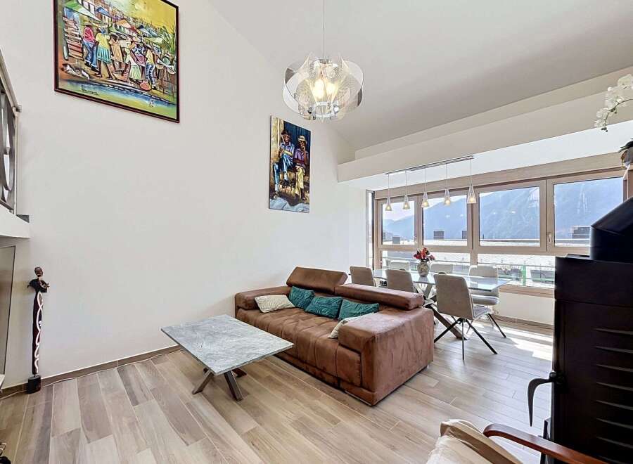 Experience modern living in this spacious apartment, featuring a comfortable brown sofa adorned with teal and cream pillows, perfect for relaxing.