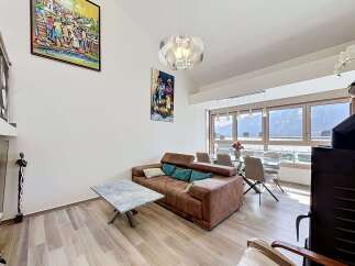 Experience modern living in this spacious apartment, featuring a comfortable brown sofa adorned with teal and cream pillows, perfect for relaxing.