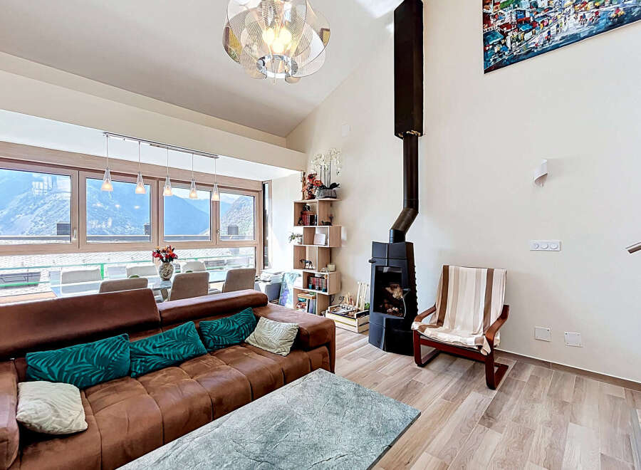 Experience breathtaking mountain views from this stunning living room, featuring a cozy brown leather sofa adorned with vibrant teal cushions.