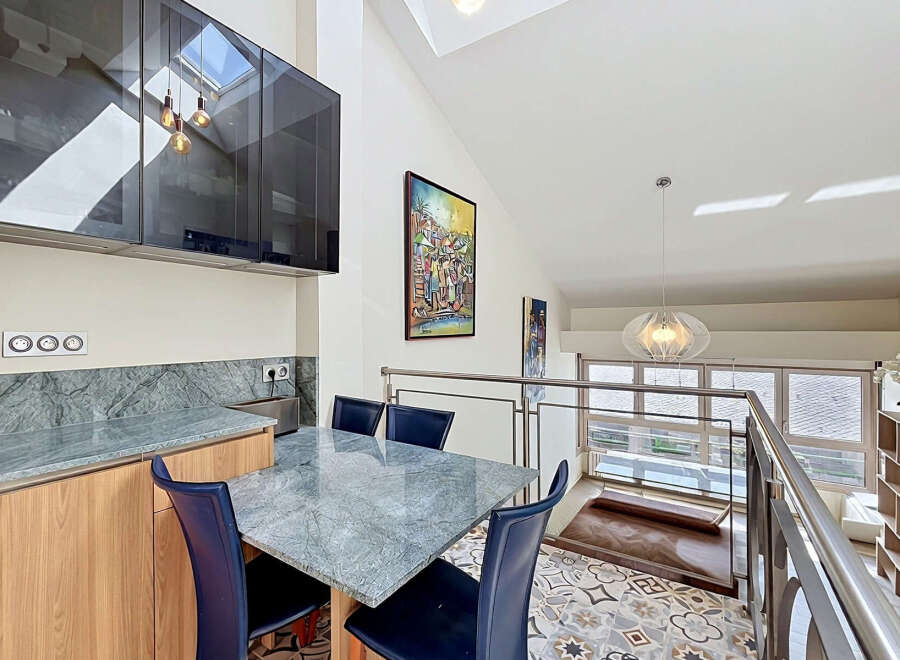 This modern kitchen and dining area features sleek, dark cabinetry with integrated lighting, complemented by a marble-patterned countertop and backsplash.