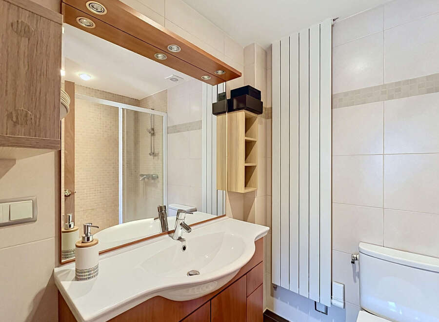This modern bathroom features a sleek vanity with a white basin and chrome faucet, complemented by warm wood cabinetry.