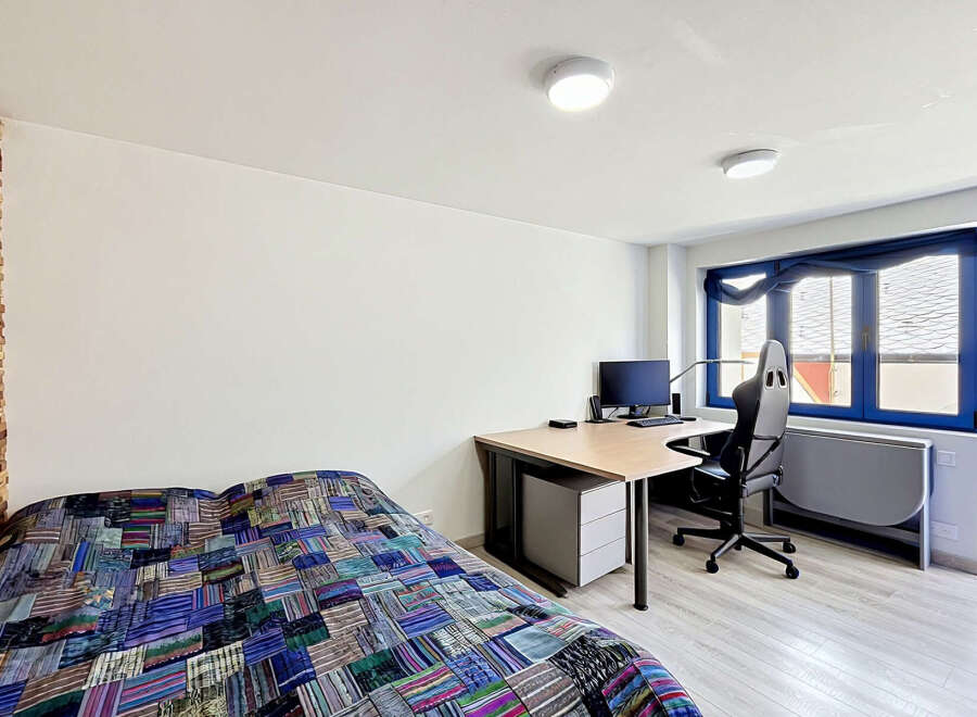 This modern studio apartment features a comfortable bed with a vibrant, patchwork quilt, perfect for relaxing after a long day.