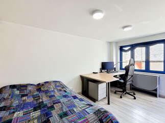 This modern studio apartment features a comfortable bed with a vibrant, patchwork quilt, perfect for relaxing after a long day.