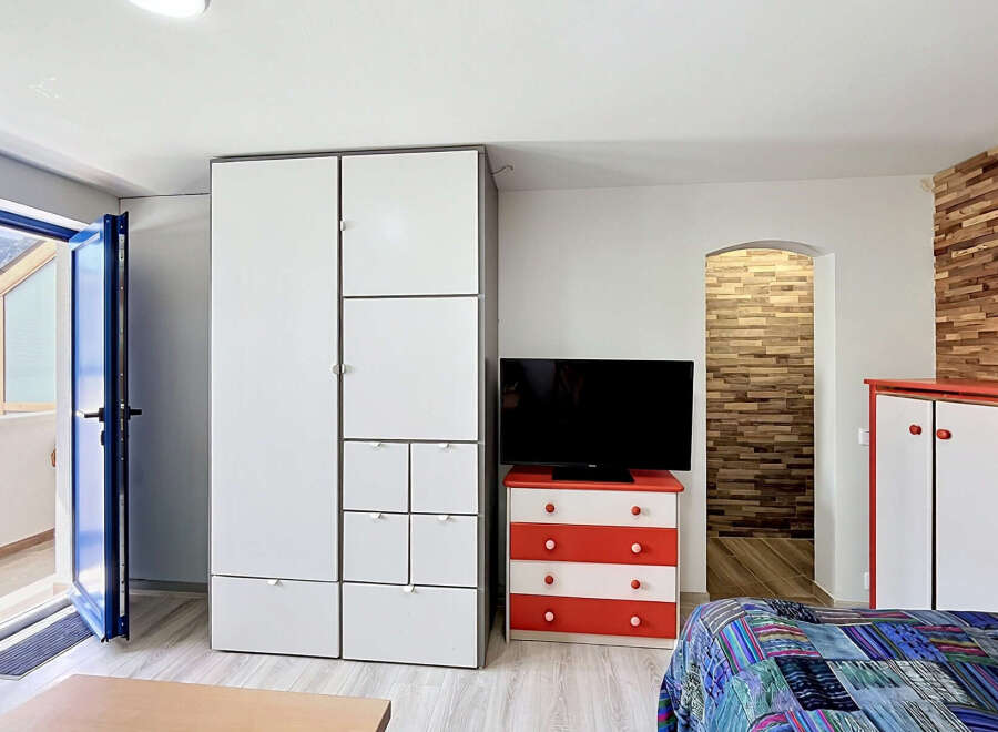 This modern studio apartment features a spacious white wardrobe and a vibrant red and white dresser, perfect for storage.