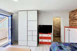 This modern studio apartment features a spacious white wardrobe and a vibrant red and white dresser, perfect for storage.