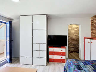 This modern studio apartment features a spacious white wardrobe and a vibrant red and white dresser, perfect for storage.
