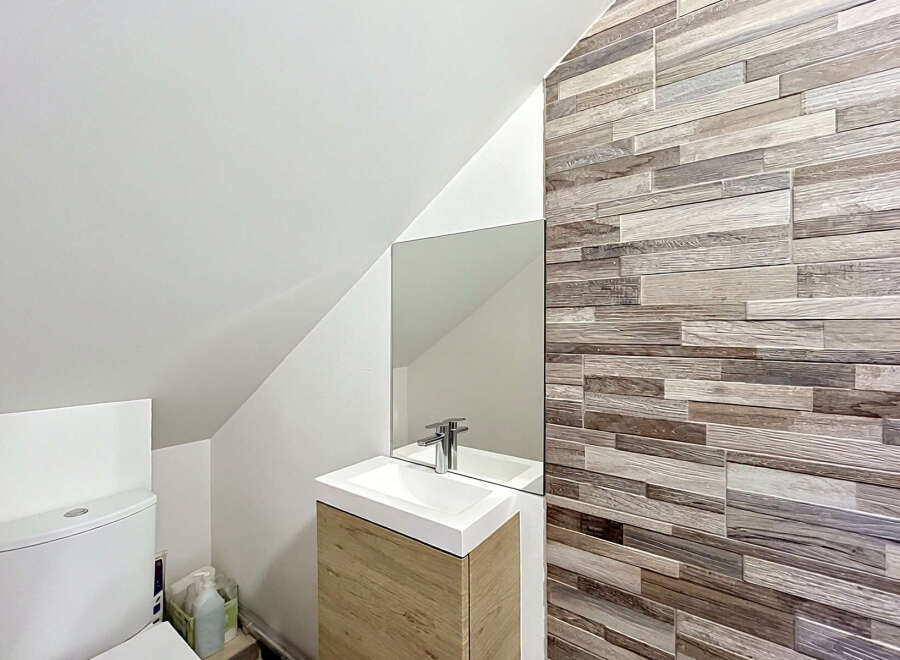 Discover this modern bathroom featuring a sleek white toilet and a stylish vanity with a wooden cabinet.
