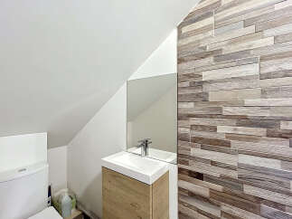 Discover this modern bathroom featuring a sleek white toilet and a stylish vanity with a wooden cabinet.