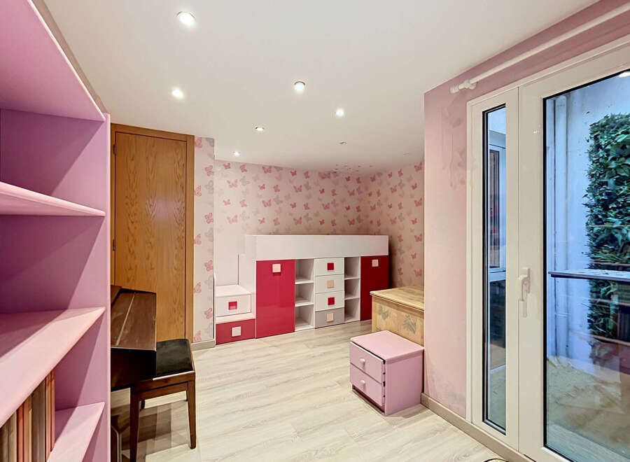 This charming children's room features a playful butterfly-themed wallpaper and a loft bed with integrated storage in vibrant pink and white.