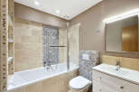 This beautifully appointed bathroom features a spacious bathtub with a glass shower screen, complemented by elegant travertine wall tiles and intricate mosaic accents.