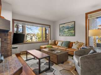 Step into this inviting living room, featuring a plush tan sectional sofa complemented by a rustic wooden coffee table and a stylish grey armchair.