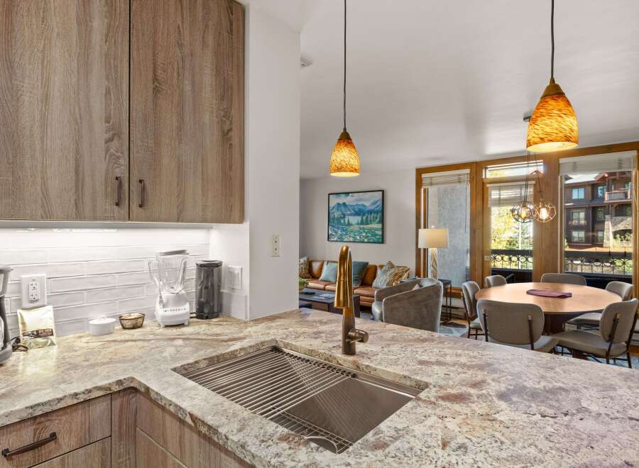 This modern kitchen boasts sleek, wood-grain cabinetry and a stunning granite countertop with an integrated sink and brass faucet.
